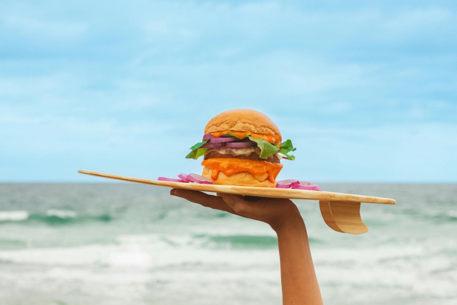 Person holding a delicious burger on the beach